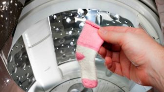 A person retrieves a single sock from the wahing machine.