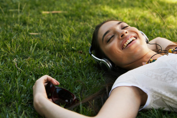 Young woman lying on grass, wearing headphones, smiling