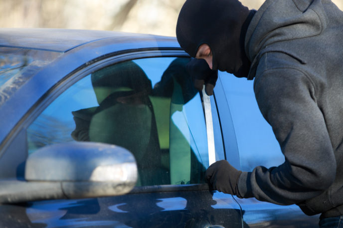 A thief using a metal rod to unlock the front door of a car