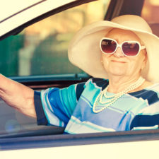 Happy senior woman in sunglasses and hat driving automobile