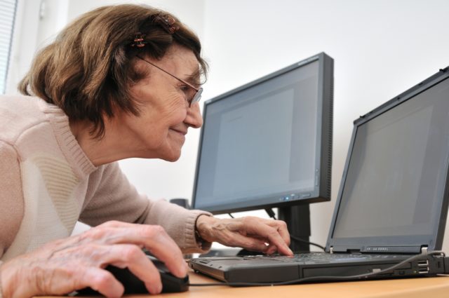80-something senior woman working with laptop, another computer in the background