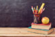 Back to school background with books, pencils and apple over chalkboard