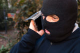 Masked thief talking on his mobile phone. Outdoors