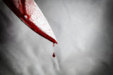 Close up of man holding knife smeared with blood and still dripping.