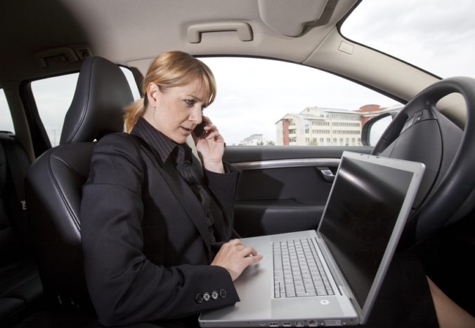 Žena za volantom telefonuje a pracuje na laptope