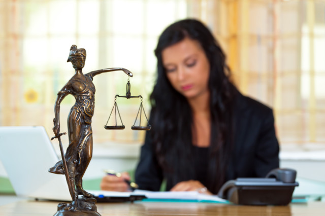 Žena sediaca za stolom so sochou spravodlivosti Justicia