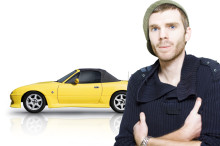 Muž v čiapke stojí pred žltým autom