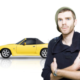 Muž v čiapke stojí pred žltým autom