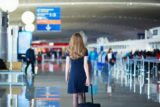 Young woman in international airport, walking with her luggage, back view. Flight attendant going to meet her crew