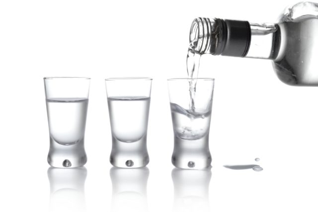 Bottle and glasses of vodka poured into a glass isolated on white