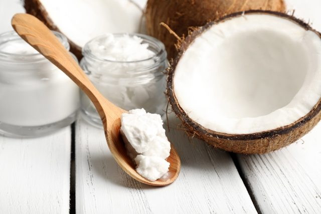 Coconut with jars of coconut oil and cosmetic cream on wooden ba
