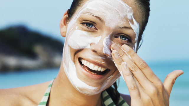 Young woman on beach, applying sunlotion on face, smiling, portrait