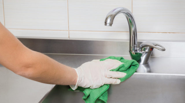 Hand in protective glove with rag cleaning kitchen equipment.