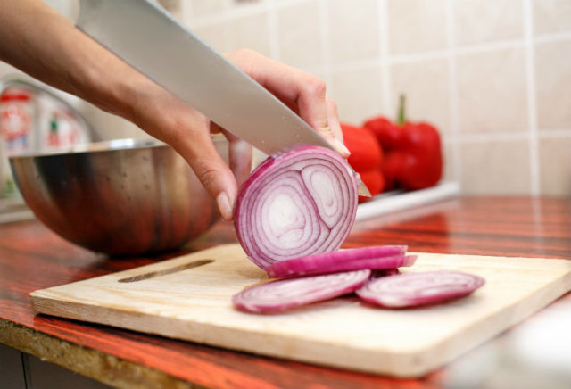 Close up of womans hand cut red onions on cutting board.jpg