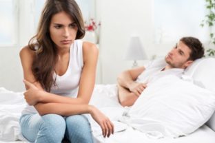 Zamyslená žena sediaca na kraji posteli chrbtom k mužovi