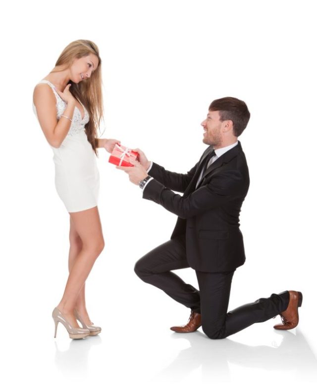 Muž kľačiaci pre ženou jej dáva červenú škatuľku