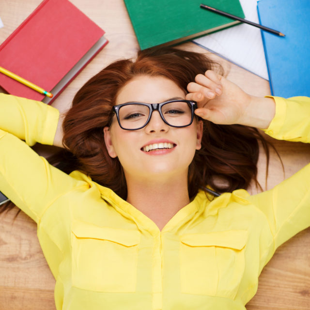 Smiling student in eyeglasses lying on floor