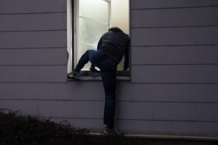 Rear View Of A Burglar Entering In A House Through A Window