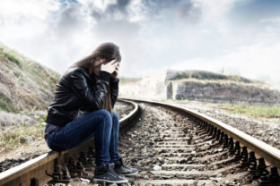 Lonely teenage girl with hands over her face sitting on the railroad