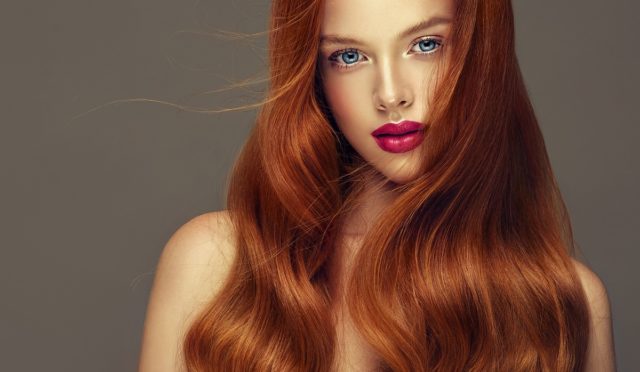 Young, red haired beautiful model with long, curly, well groomed hair. Irish beauty. Excellent hair waves. Hairdressing art and hair care.