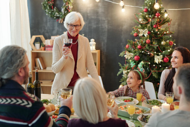 Happy senior woman with glass of wine making Christmas toast by family dinner