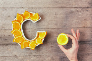 Vitamin C or Ascorbic acid nutrient in food concept. Plate in shape of letter C with orange slices and woman's hand with citrus making sign OK on wooden background. Flat lay or top view.
