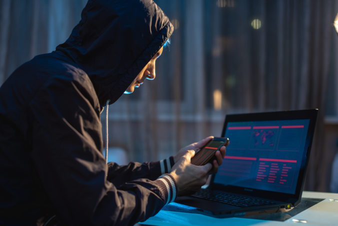 Male hacker in the hood holding the phone in his hands trying to steal access databases. Concept of cybersecurity