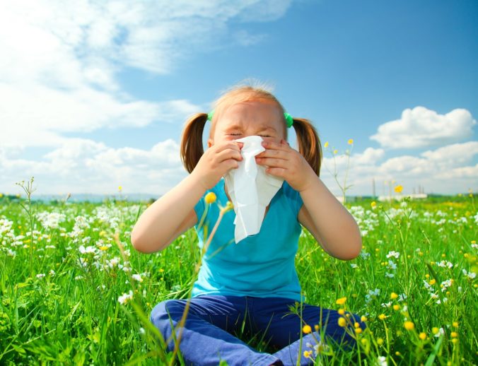 Little girl is blowing her nose while sitting on green meadow