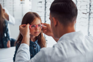 Young pediatrician in white coat helps to get new glasses for little girl