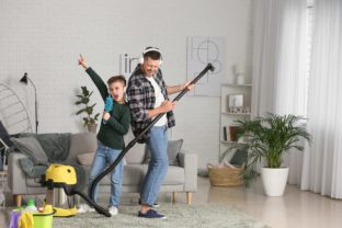 Little boy and his father having fun while hoovering floor in room