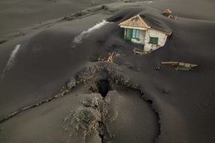 FILE - A fissure is seen next to a house covered with ash on the Canary island of La Palma, Spain, Dec. 1 2021. A volcanic eruption in Spain’s Canary Islands shows no sign of ending after 85 days. It became the island of La Palma’s longest eruption on record on Sunday, Dec. 12.