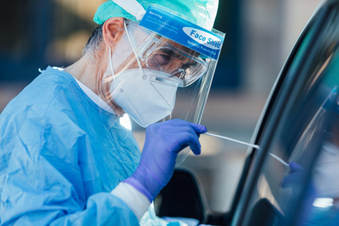 Medical personnel wearing a PPE, performing PCR with a swab in their hand, on a patient inside his car to detect if he is infected with COVID 19