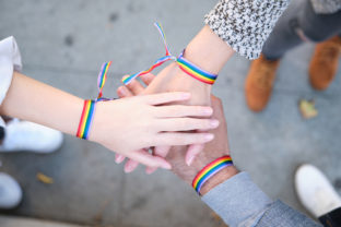 Hands of a group of three people with LGBT flag bracelets