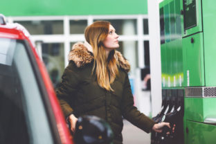 Young caucasian woman at self service gas station, hold fuel nozzle and refuel the car with petrol, diesel, gas. Pretty woman filling her auto with gasoline or benzine, outdoors. Self service gas pump