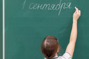 School teacher young woman in a white blouse in the classroom on a blackboard writes with chalk. translation - September 1. portrait