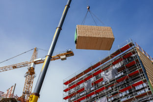 Crane lifting a prefabricated wooden building module to its position in the structure.