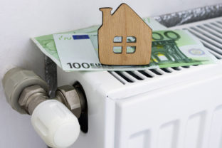 A small wooden house on the background of euro banknotes and radiator heating. Payment for heating in winter. Symbolic image, selective focus.