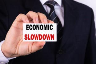 A businessman is holding a tablet with the text Economic Slowdown in front of him in his hands. Business concept