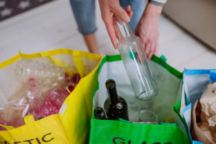 Midsection of woman throwing empty glass bottle in recycling bin in kitchen.