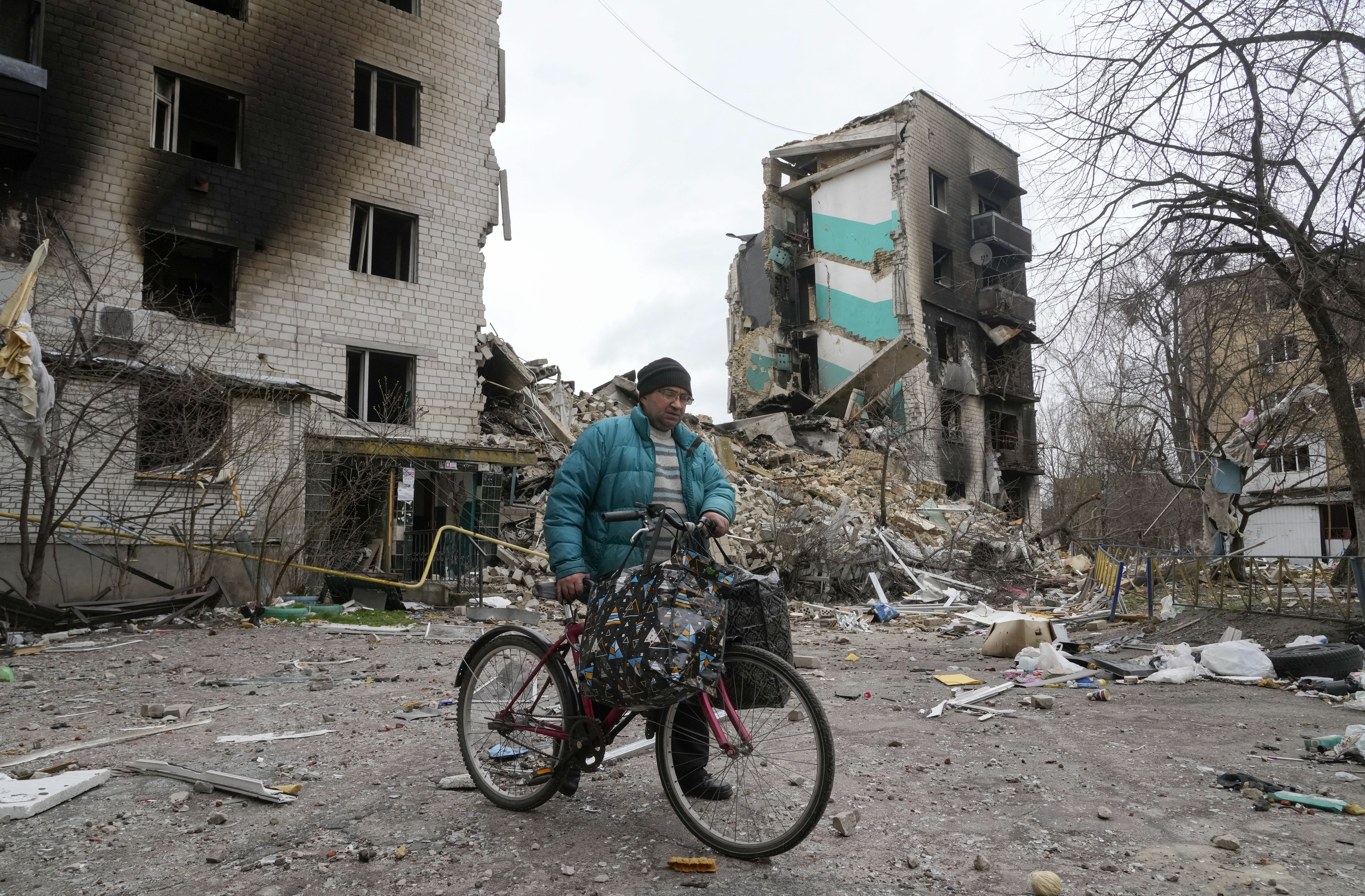 Russia Ukraine War A man carries his belongings on a bike as he leaves his house, background, ruined in the Russian shelling in Borodyanka, Ukraine, Wednesday,