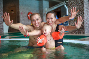 Happy family relaxing in the spa center with a child swims in th