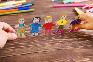 The child does figures of people of paper. Paper people on wooden background. Creative child play with craft.
