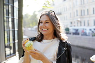 Cheerful overjoyed pleased mature woman with stylish black leather jacket on her shoulders laughing, having fun outdoors, enjoying tasty delicious ice cream in waffle cone, smiling broadly