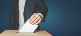 Unrecognizable male voter holds in his hand a ballot above the ballot box