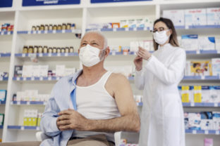 Therapy in a nursing home pharmacy. Female pharmacist gives therapy to a senior man who is sitting on a chair and has taken off his shirt. Vaccination, corona virus breaking news