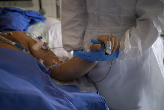 A doctor wearing protective gear holds the hand of a patient at the intensive care unit of Honved Hospital treating COVID-19 patients
